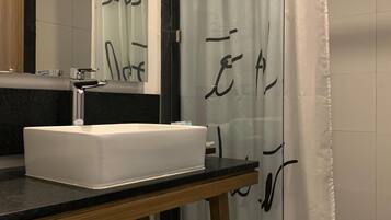 A bathroom with a white sink, a mirror, a towel, and a shower curtain with black text.