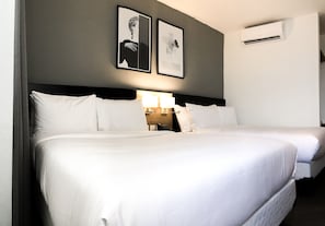 A hotel room with two beds, a nightstand with a lamp, and framed pictures on the wall.