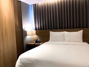 A hotel room with a wooden headboard, a bedside table with a lamp, a phone, and a bed with white bedding.