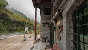 Un edificio de piedra con un porche, una banca y vistas a una carretera y vegetación.