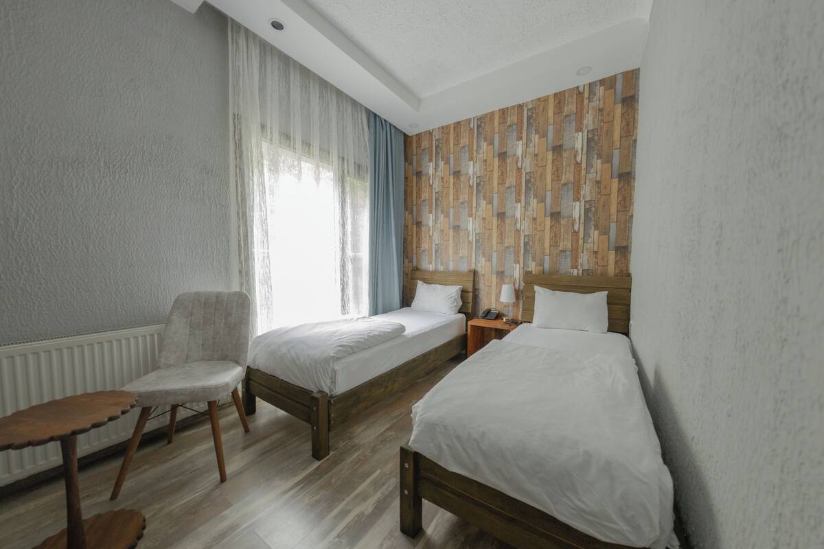 A hotel room with two beds, a chair, a small table, and a wooden-patterned wall.