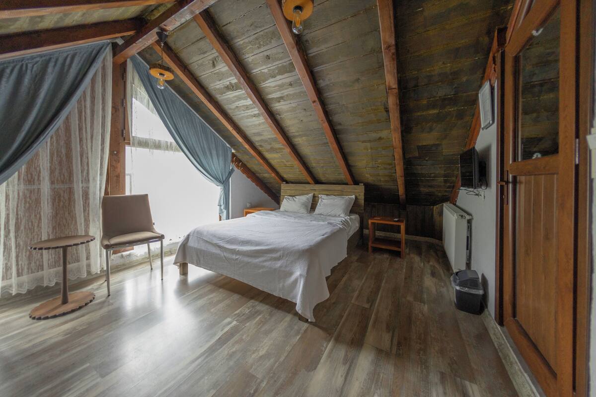 A bedroom with a wooden ceiling, a bed, a chair, and a window.