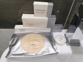 Un baño con lavamanos, espejo y artículos de aseo personal, incluyendo una bolsa sanitaria, kit de afeitado, kit dental y jabón facial.