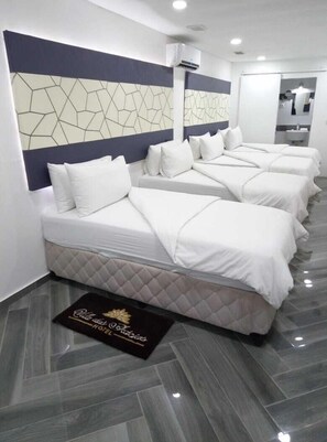 A hotel room with four beds, a modern design, a geometric wall pattern, and a black doormat with gold lettering. - Vila das Acácias (Maputo)