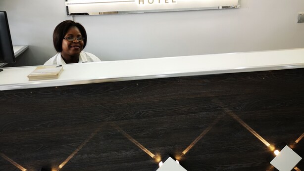 A reception desk at Vila das Açacias Hotel with a modern design, a logo above the desk, and a dark wood paneling. - Vila das Acácias (Maputo)