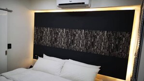 A modern hotel room with a large bed, white bedding, a stone-textured headboard, and an air conditioning unit above the bed. - Vila das Acácias (Maputo)