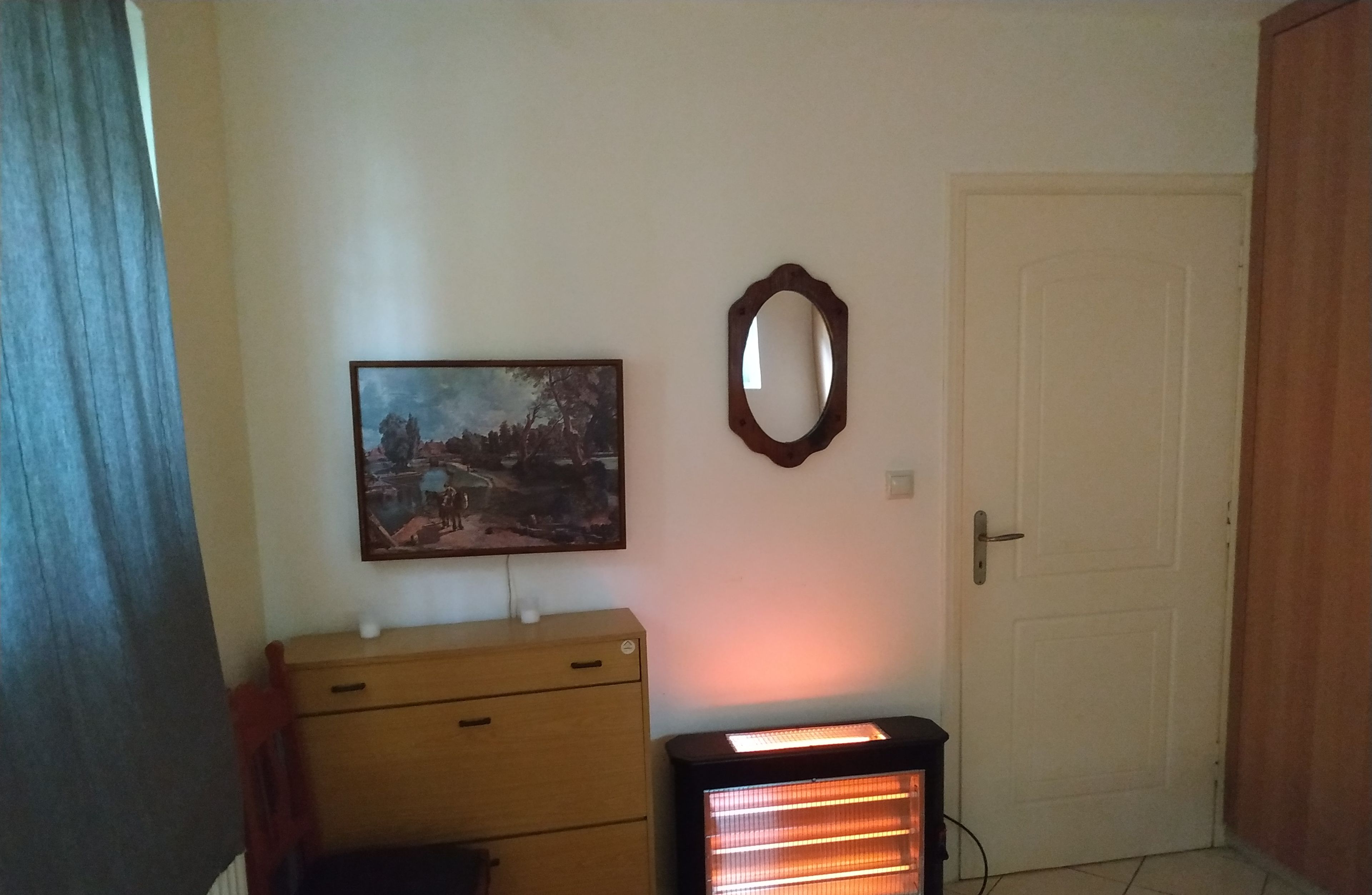 Una habitación con un armario de madera, un cuadro, un espejo y un calentador.