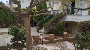 A courtyard with a tree, gravel paths, and a building with balconies. - Stavros Apartments (Spata-Artemida)