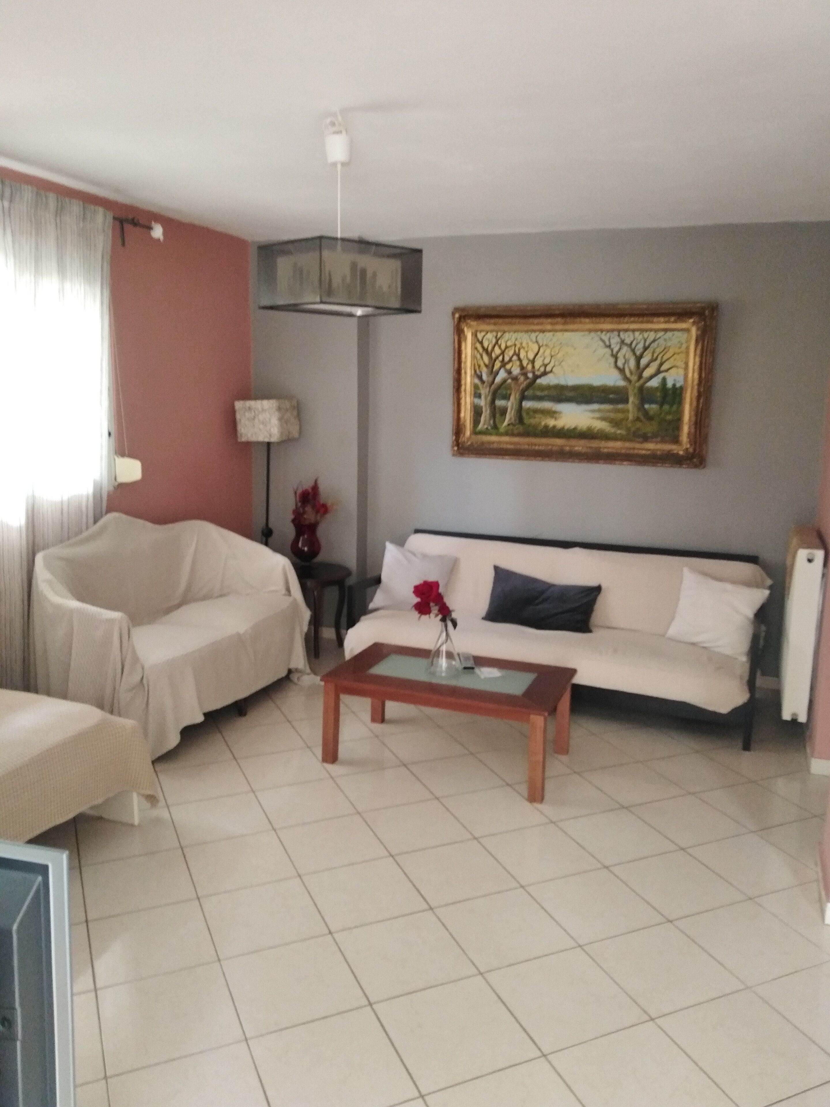 Una sala de estar con un sofá, una mesa de centro con un florero, una lámpara y un cuadro en la pared.