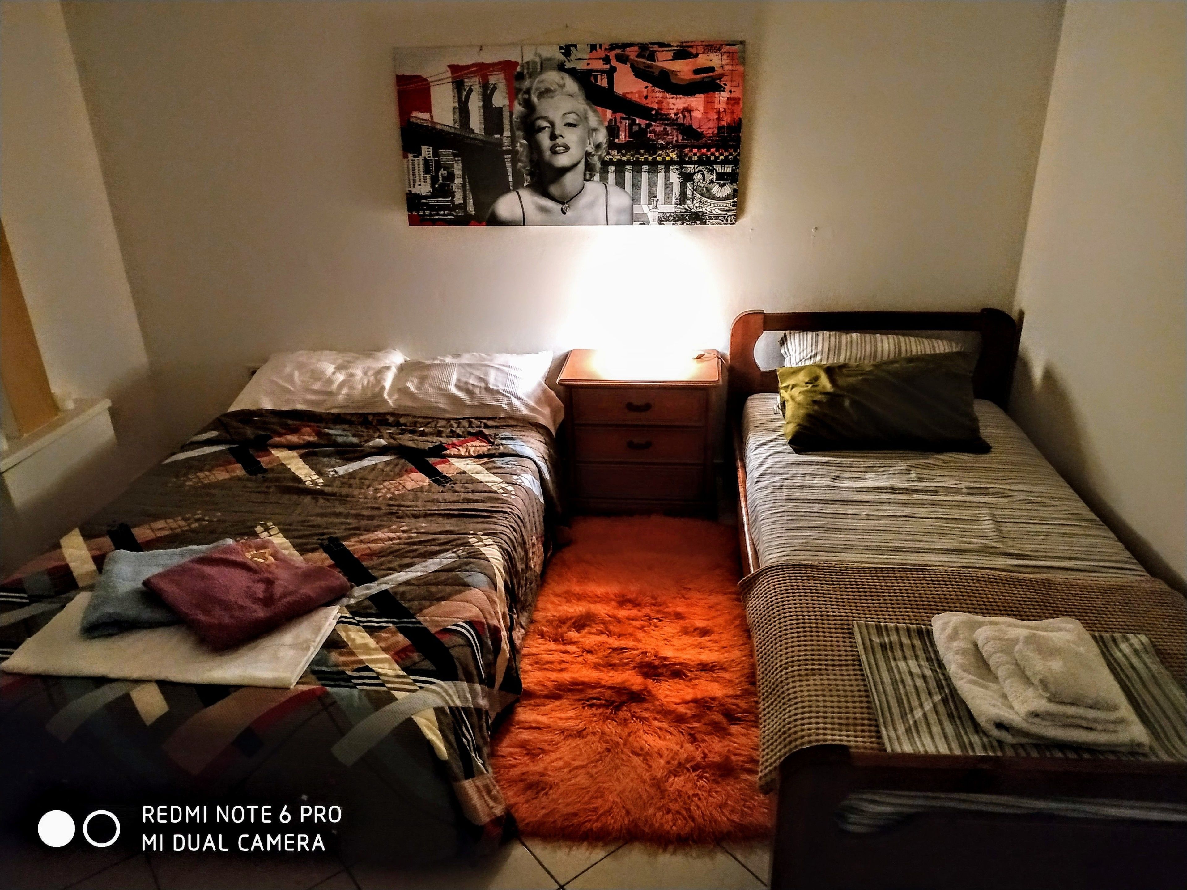 Ein Schlafzimmer mit zwei Betten, einem Nachttisch, einem Teppich und einem Wandbild.