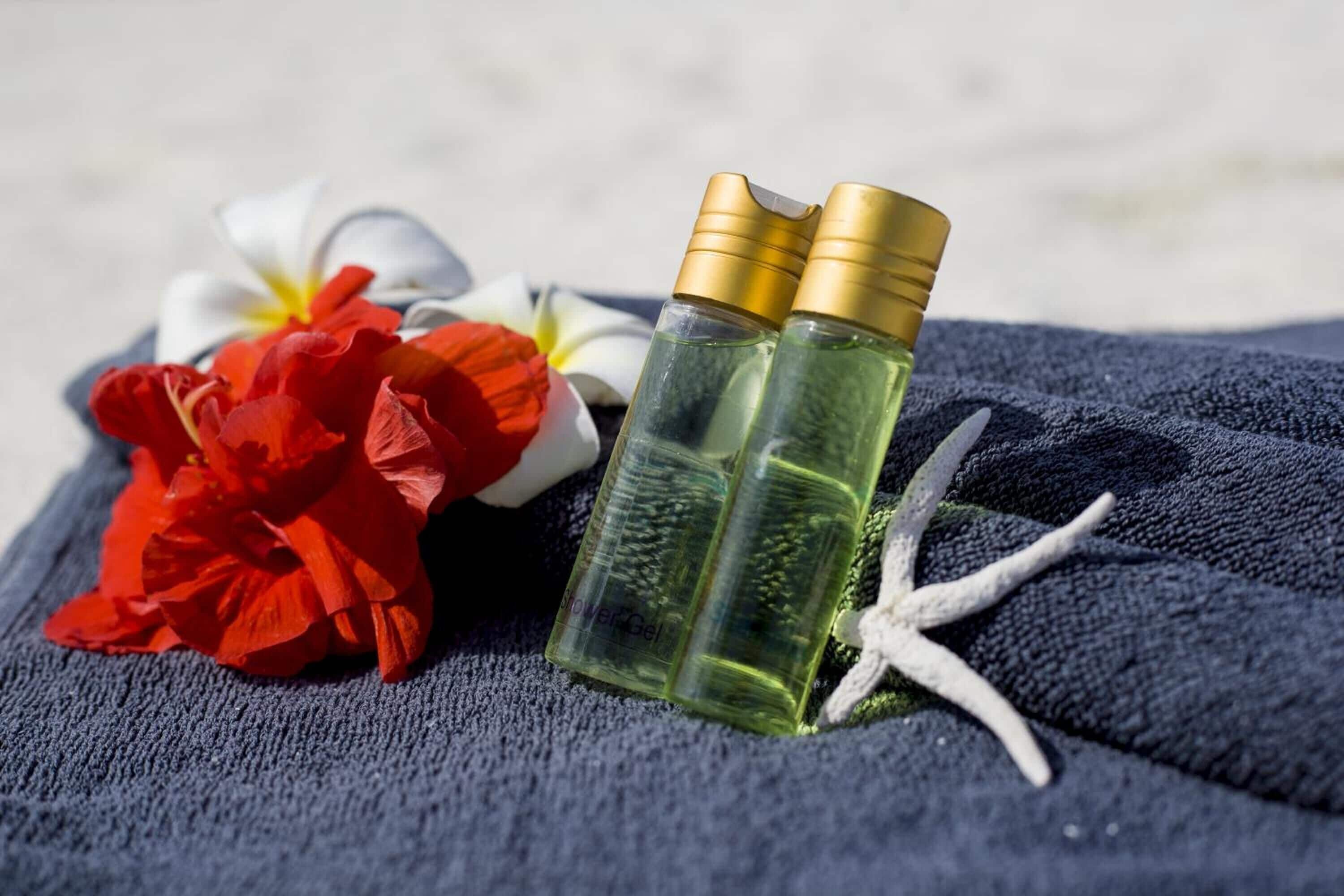 Two clear glass bottles with gold caps, a red flower, and a white flower on a dark fabric.