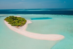 Vue aérienne d’une île tropicale avec une étroite plage de sable, une végétation luxuriante et une eau turquoise cristalline.