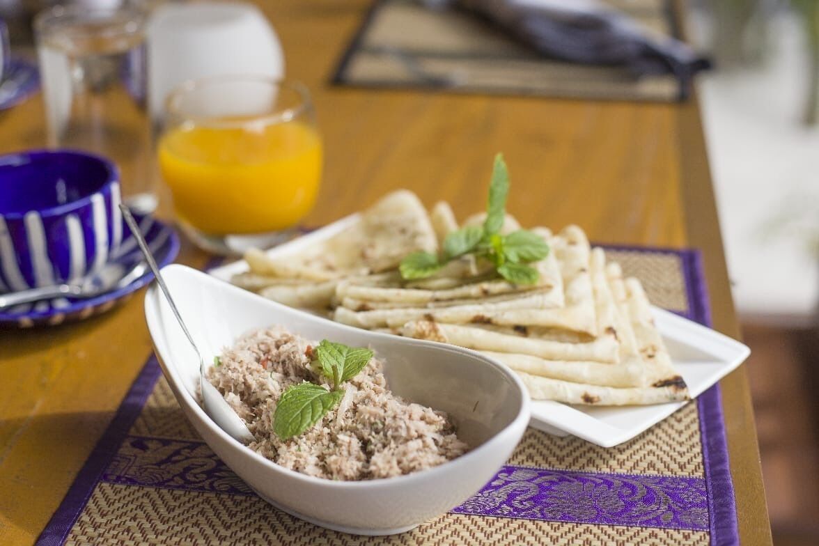A table with a plate of flatbreads, a bowl of rice dish, and a glass of orange juice.