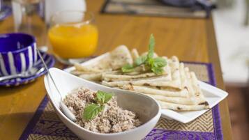 A table with a plate of flatbreads, a bowl of rice dish, and a glass of orange juice.