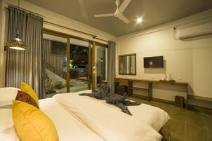 Habitación de hotel con cama, escritorio, televisión y puerta corrediza de vidrio que da a un espacio exterior.