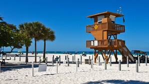 Una torretta di salvataggio su una spiaggia sabbiosa, con palme e ombrelloni sullo sfondo.