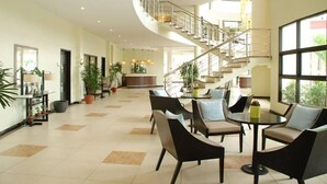 A spacious lobby with a curved staircase, seating area, and potted plants.