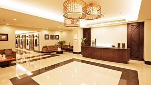 A spacious lobby with a reception desk, seating area, and a modern chandelier.