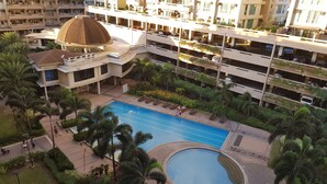 A multi-story hotel with a central swimming pool, surrounded by palm trees and greenery.
