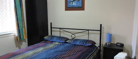 Un dormitorio con una cama, un radiador negro, un cuadro en la pared y una ventana con cortinas.
