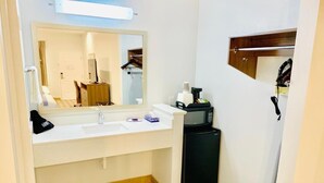 A compact bathroom with a white sink, a mirror, a black refrigerator, and a wooden shelf. - Porter Inn (Porter)