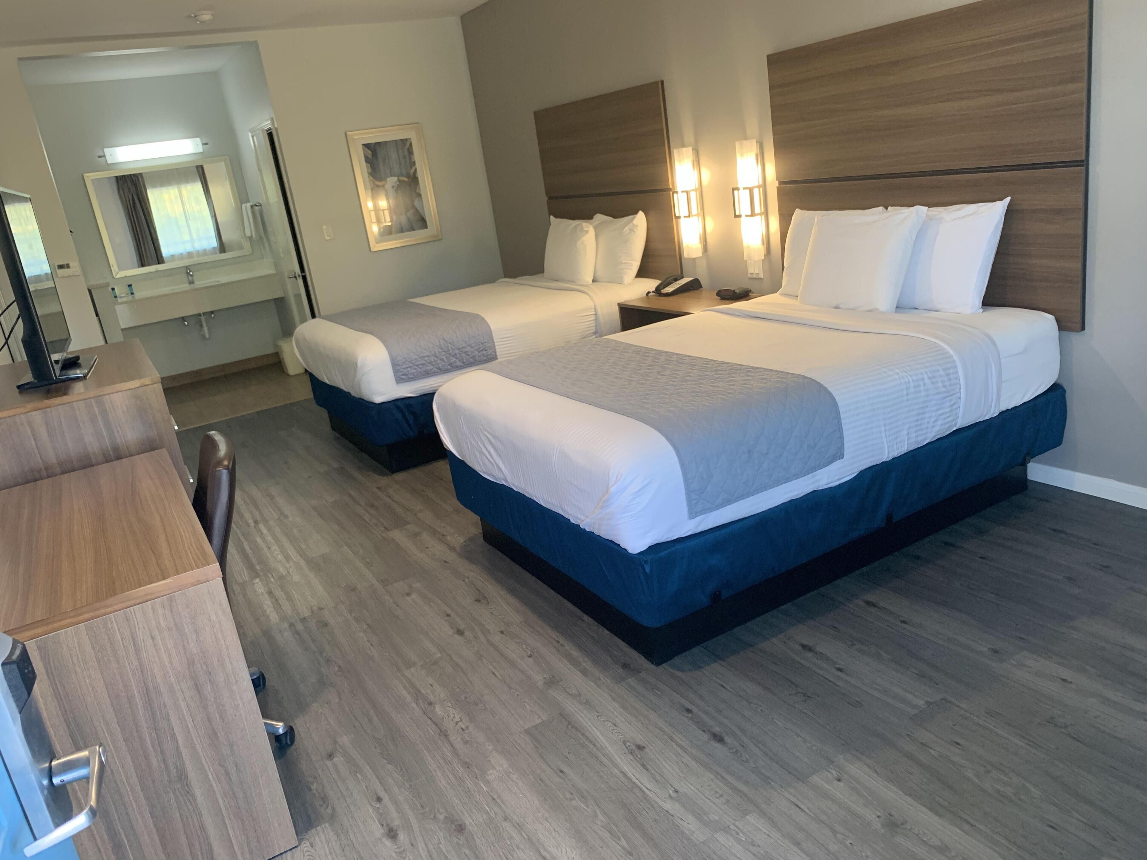 Habitación de hotel con dos camas, un escritorio, una silla y un espejo.