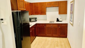 A compact kitchen with wooden cabinets, a black refrigerator, a microwave, and a coffee maker. - Porter Inn (Porter)