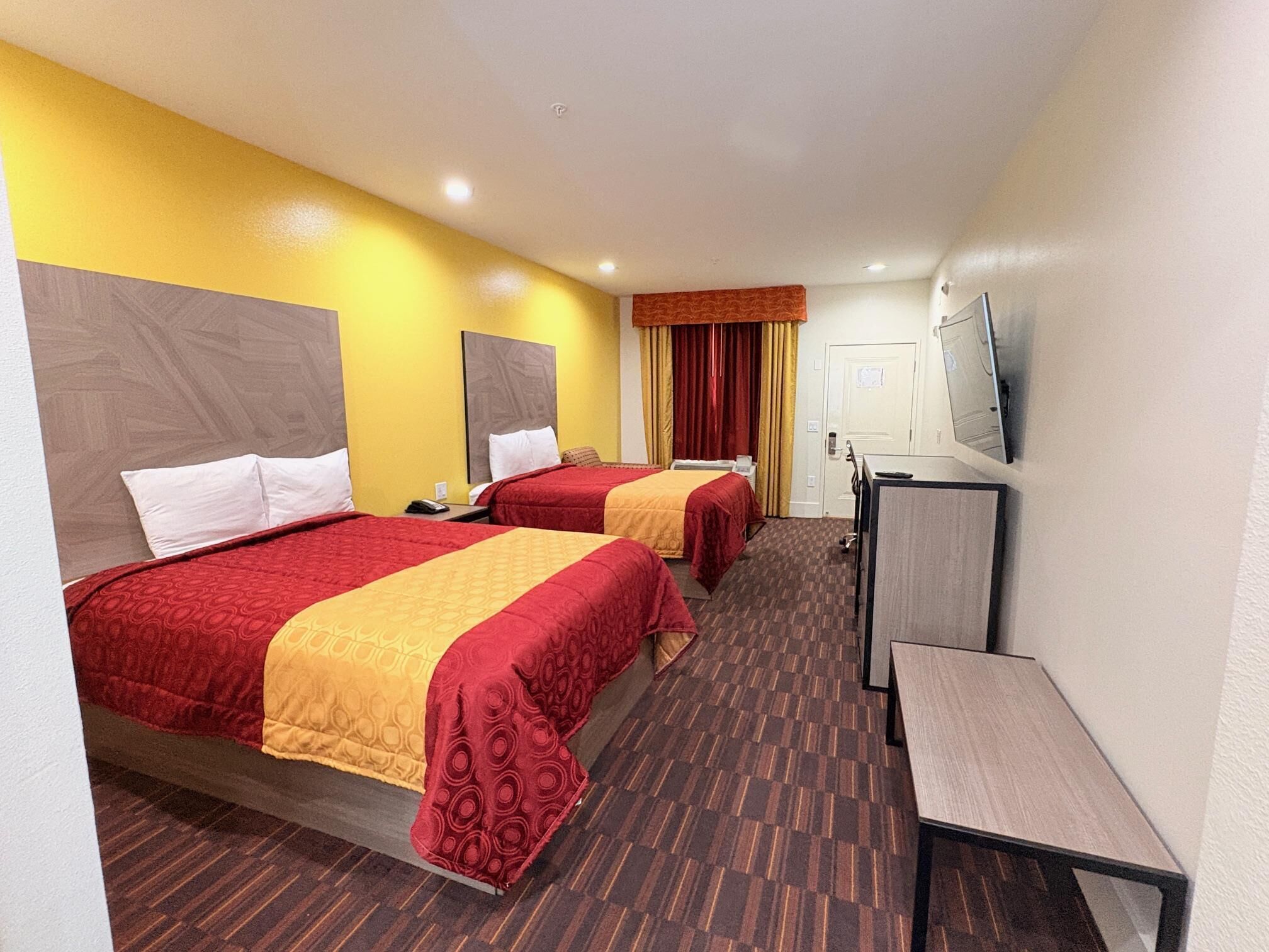 A hotel room with two beds, a desk, a television, and a door.