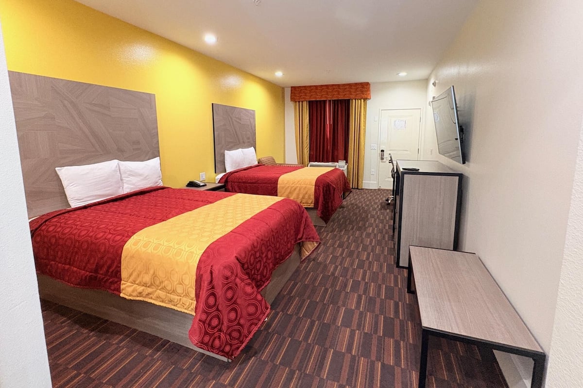 Habitación de hotel con dos camas, un escritorio, un televisor y una puerta.
