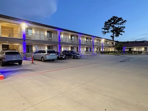 A motel with multiple rooms, a parking lot, and a tree in the background. - Americas Best Value Inn & Suites Houston Veterans Memorial (Houston)