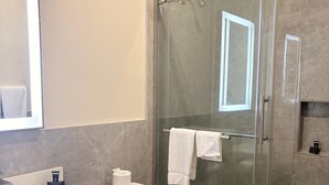 A modern bathroom with a glass-enclosed shower, a white toilet, and a countertop with a soap dispenser and a tissue box. - Americas Best Value Inn & Suites Houston Veterans Memorial (Houston)
