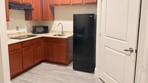 A compact kitchen with wooden cabinets, a black refrigerator, a microwave, and a stainless steel sink. - Americas Best Value Inn & Suites Houston Veterans Memorial (Houston)