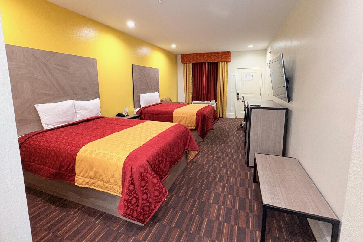 Een hotelkamer met twee bedden, een bureau, een televisie en een deur.