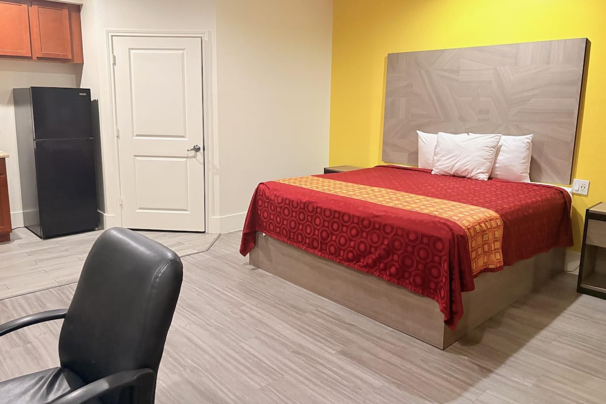 Una habitación de hotel con una cama, una silla, un escritorio, un refrigerador y una puerta.