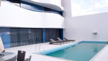Uma área de piscina moderna ao ar livre com guarda-corpo de vidro, espreguiçadeiras e uma mesa.