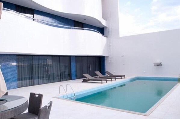 A modern outdoor pool area with a glass balustrade, lounge chairs, and a table.