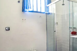A bathroom with a glass shower enclosure, a white sink, and a window with blue curtains. - Ilha Bela a Beira Mar (Ilhabela)