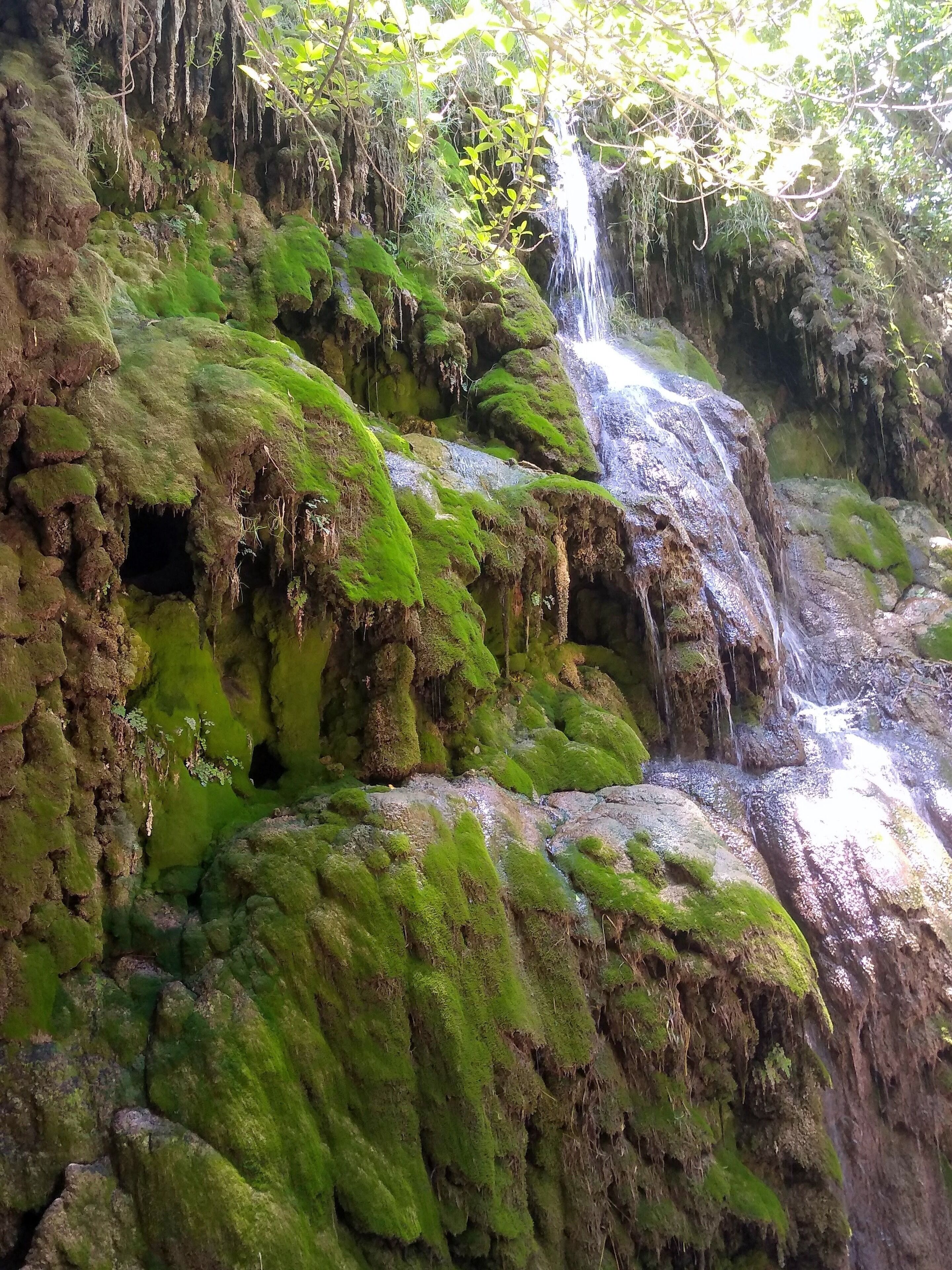 A natural rock formation with a waterfall and moss-covered surfaces.