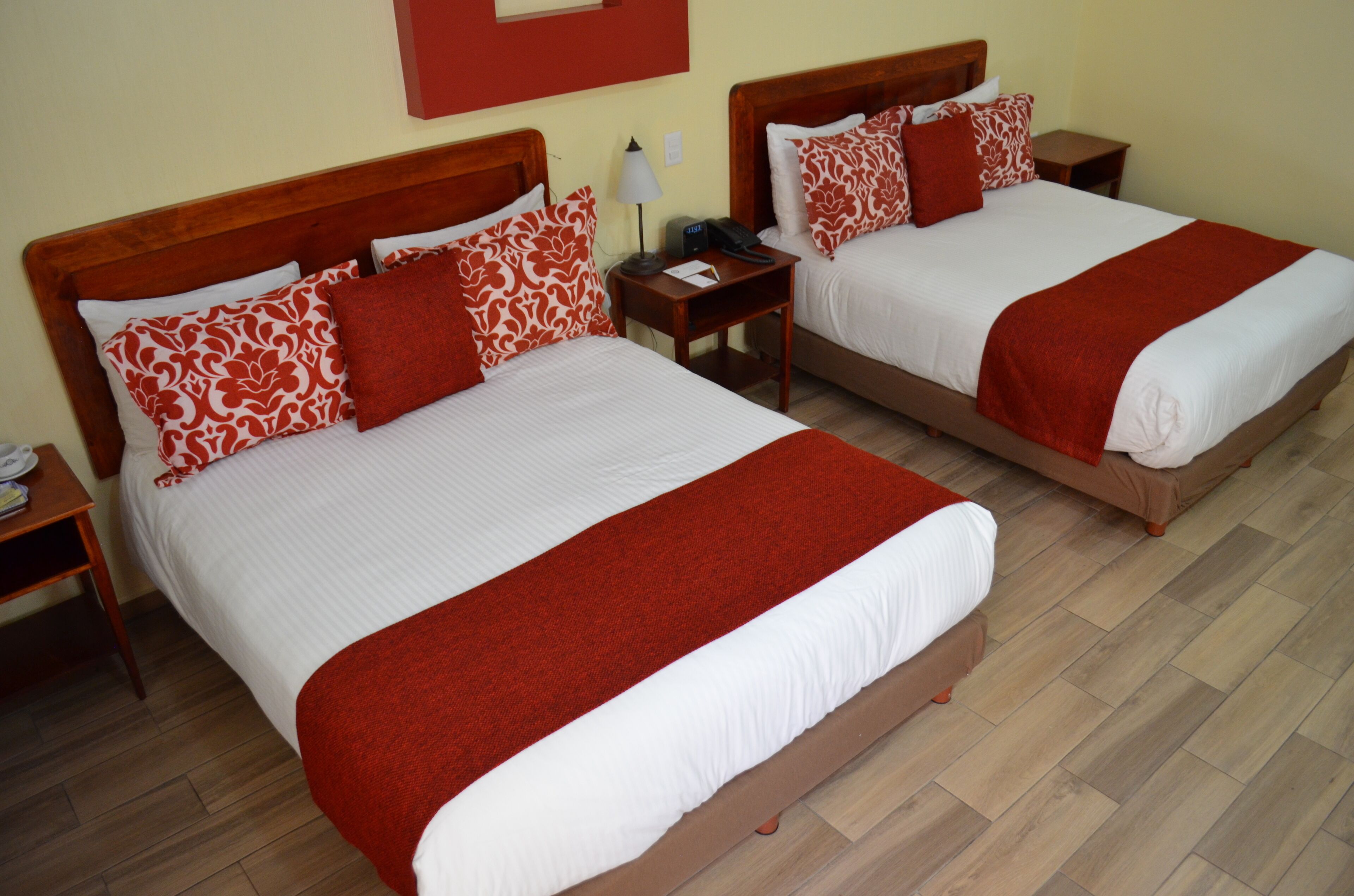 Two double beds with red and white bedding, wooden headboards, and bedside tables with lamps and phones.