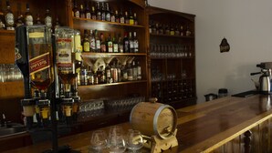 Zona de bar con mostrador de madera, un barril grande de madera y una variedad de botellas de licor y vasos.