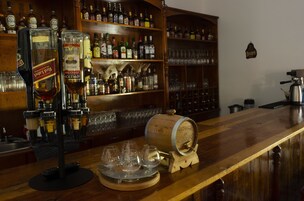 A bar area with a wooden counter, a large wooden barrel, and a variety of liquor bottles and glasses.