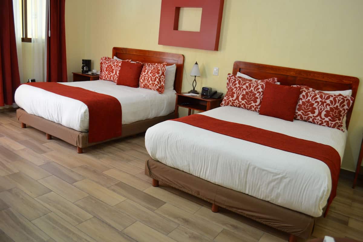 Two double beds with red and white bedding, wooden headboards, bedside tables with lamps, and a wooden floor.