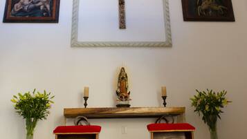 Innenansicht einer Kirche mit Kruzifix, zwei Holzbänken und gerahmten religiösen Bildern.