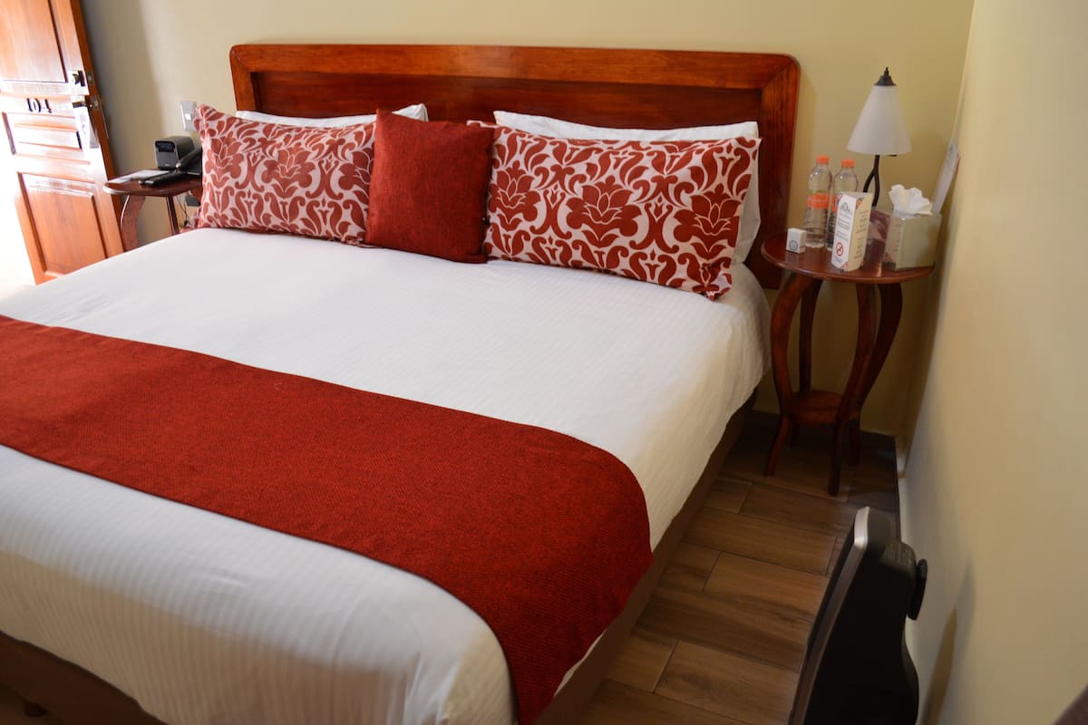 A hotel room with a large bed, wooden headboard, and a nightstand with a lamp and toiletries.