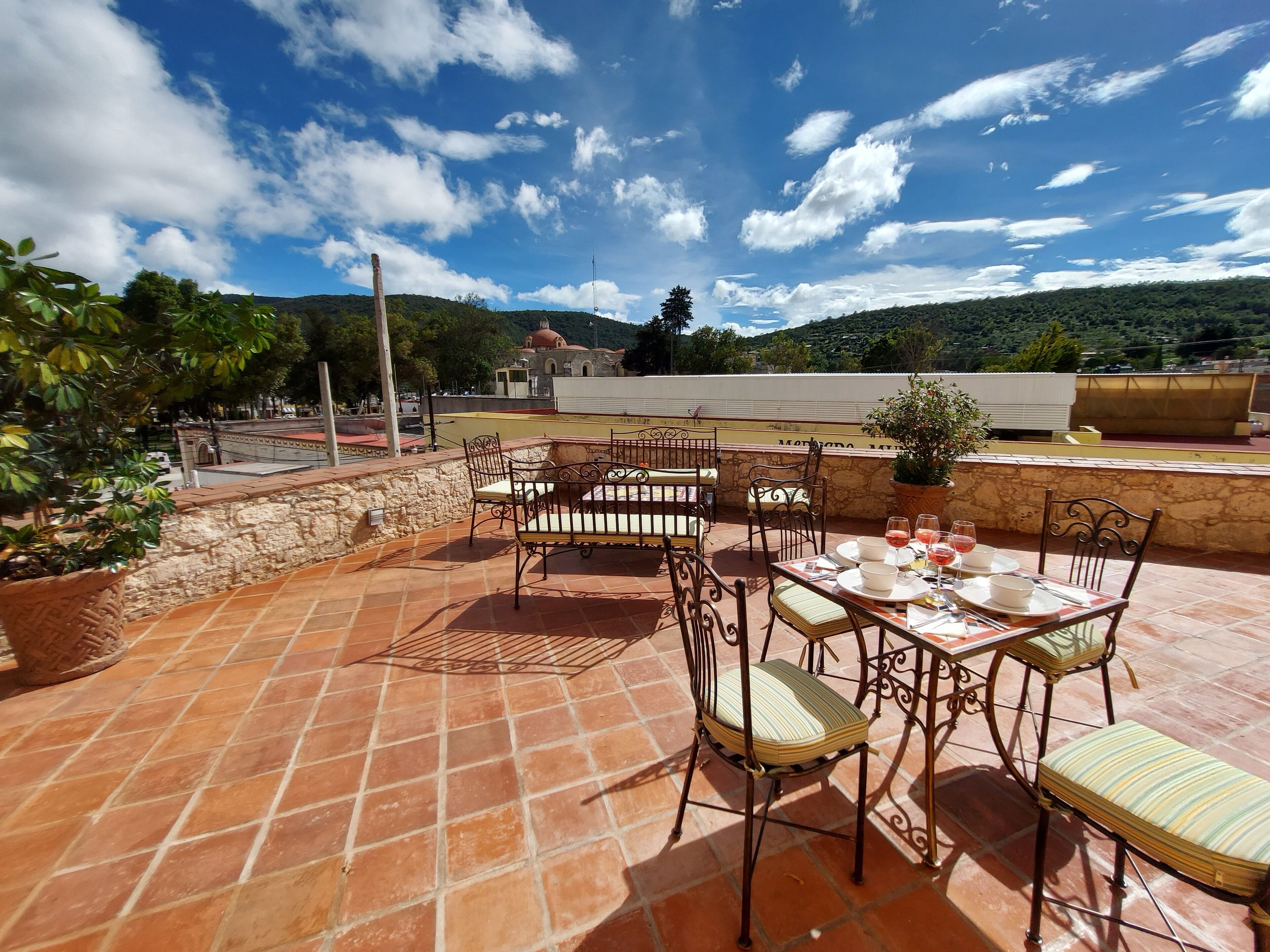 A terrace with outdoor seating, stone walls, and a view of a church and hills.