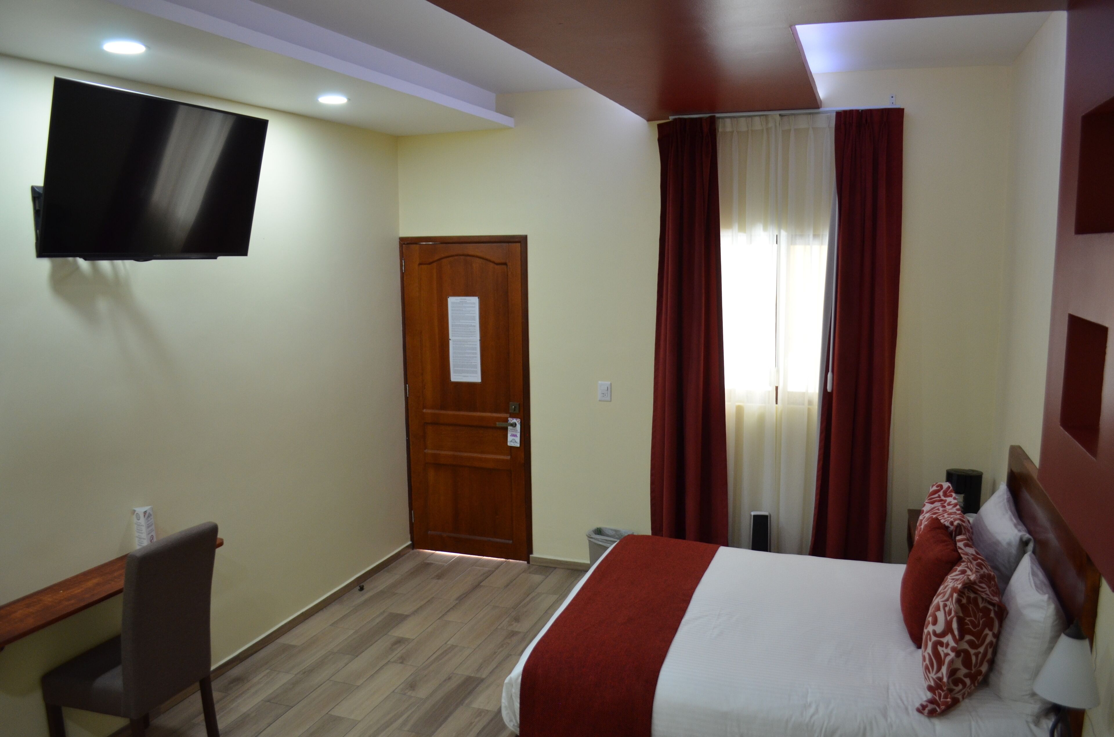 A hotel room with a bed, a desk, a chair, a television, and a door.
