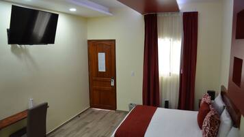 A hotel room with a bed, a desk, a chair, a television, and a door.