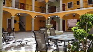 Un patio de varios niveles con una fuente central, zonas de estar y una escalera que conduce a un nivel superior.
