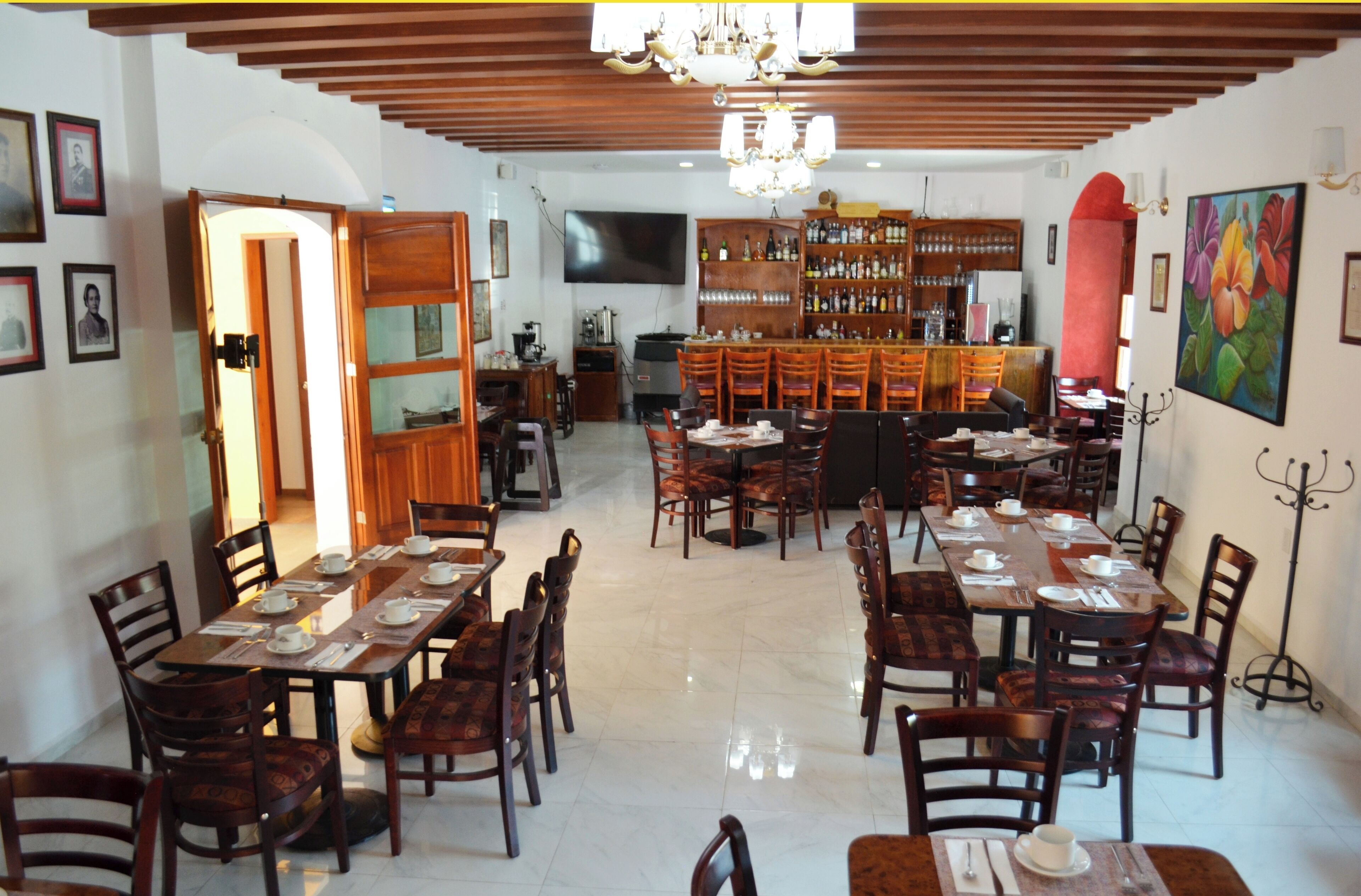 A dining area with multiple tables and chairs, a bar area with shelves of bottles, and a television mounted on the wall.