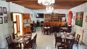 Un comedor con varias mesas y sillas, una zona de bar con estantes llenos de botellas, y un televisor colgado en la pared.